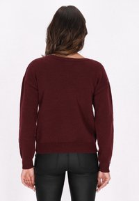 Pulover tricotat burgundy cu decolteu larg și mâneci lungi, având manșete și margine ribbate. Textură netedă, croială lejeră.