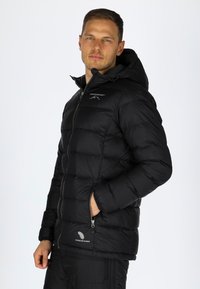 Svart puffjacka med huva, med quiltat mönster, fickor med dragkedja och "Premium Down"-logga på nederkanten. Snygg och lätt.