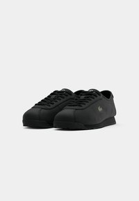 Pair of black low-top sneakers with lace-up design and small logo on the side, set against a plain light background.