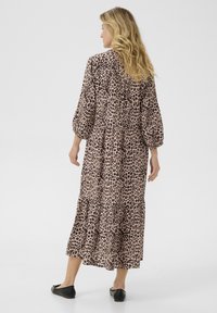 Haljina dugog kroja s leopard uzorkom, izrađena od lagane tkanine, s napućenim rukavima, višeslojnim suknjom i opuštenim siluetom. Vidljive crne balerinke.
