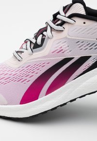 Ljust rosa och vit löparsko med svarta och magenta detaljer, vita snören och en strukturerad vit mellansula.