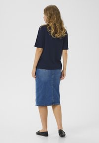 Marinblå kortärmad topp tillsammans med en knälång denimkjol. Kjolen har rak skärning och slits bak. Modellen bär svarta ballerina-skor.