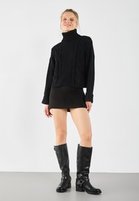 Pull en maille torsadée noir avec une coupe ample, associé à une mini-jupe noire et des bottes en cuir noir montant jusqu'aux genoux avec des boucles.