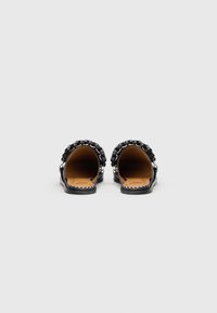 Pantofi negri cu spate deschis, prezentând un design împletit al brâului superior, material din piele netedă și o talpă plată cu accente detaliate de cusătură.