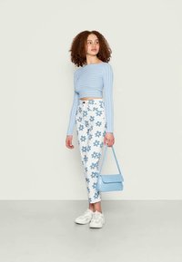Top cropped de manga longa azul claro com textura, combinado com calças brancas de cintura alta com padrões florais azuis, complementado por uma pequena bolsa azul.