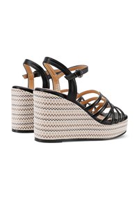 Sandali wedge neri in pelle con design a strisce, piattaforma intrecciata in beige e marrone, cinturino alla caviglia regolabile e dettagli testurizzati.