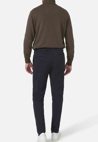 Bruine coltrui en marineblauwe chino's, met een slanke pasvorm en achterzakken met rits, gecombineerd met witte sneakers.