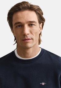 Marineblå sweatshirt med rund hals og hvid indvendig krave, lavet af blødt stof med en lille broderet logo på brystet.