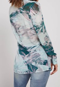 Blusa a maniche lunghe in tessuto traslucido con un motivo floreale pastello e accenti circolari, in tonalità di azzurro e verde, con una vestibilità rilassata.