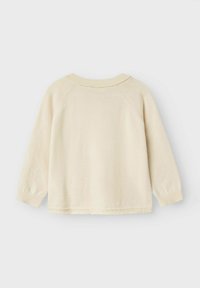 Pull en tricot de couleur crème avec des manches longues, un col rond et des poignets côtelés. Le tissu est doux, présentant une texture lisse avec des coutures minimales.