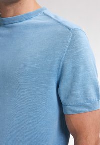 Tricou scurt cu mânecă, de culoare albastru deschis, realizat dintr-un material moale, cu textură. Este dotat cu un gât rotund și detalii rib în jurul mânecilor și gâtului.