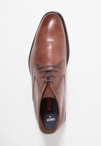 Chaussure habillée pour homme en cuir marron avec des lacets bleus, bout arrondi et semelle noire, vue de dessus sur fond blanc.