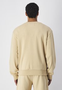 Sudadera beige con cuello redondo, puños y dobladillo acanalados. Textura suave, corte relajado y detalles mínimos en la espalda.