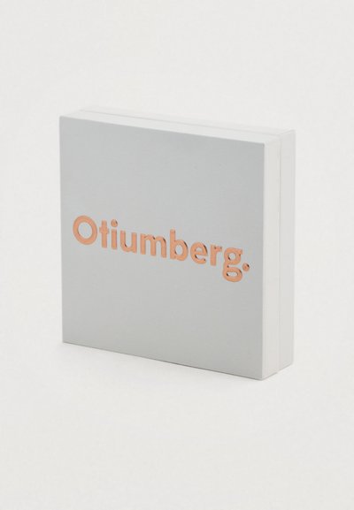 Τετράγωνο κουτί σε ματ λευκό, με τη λέξη "Otiumberg." σε ανάγλυφη ροζ χρυσή απόχρωση μπροστά, με ομαλή υφή και μινιμαλιστικό σχέδιο.
