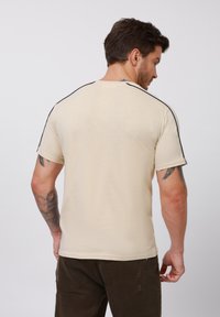 Beige T-Shirt mit kurzen Ärmeln und schwarzen Akzentnähten an den Schultern. Glattes Material, klassischer Schnitt und runder Halsausschnitt. Keine sichtbaren Logos.