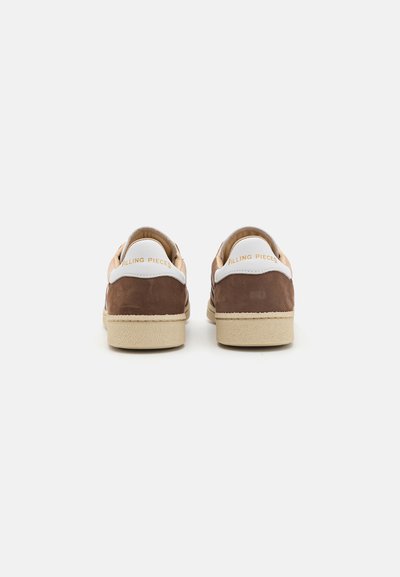 Zapatillas de ante marrón con suela de goma beige y acentos de cuero blanco, con el logo de "Filling Pieces" en el talón.