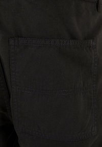 Pantaloni cargo din bumbac negri, cu un buzunar mare, pătrat la spate, cu detalii de cusătură vizibile, textură netedă și un design clasic.