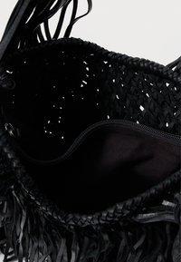 Bolsa tecida preta com detalhes em franjas, apresentando uma camada exterior texturizada. O interior é forrado com tecido preto e possui um bolso com fecho.