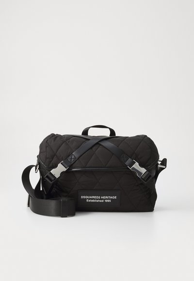 Sac à épaule noir matelassé avec des sangles croisées, de forme rectangulaire et avec un patch de marque. Texture lisse, accents en métal argenté.