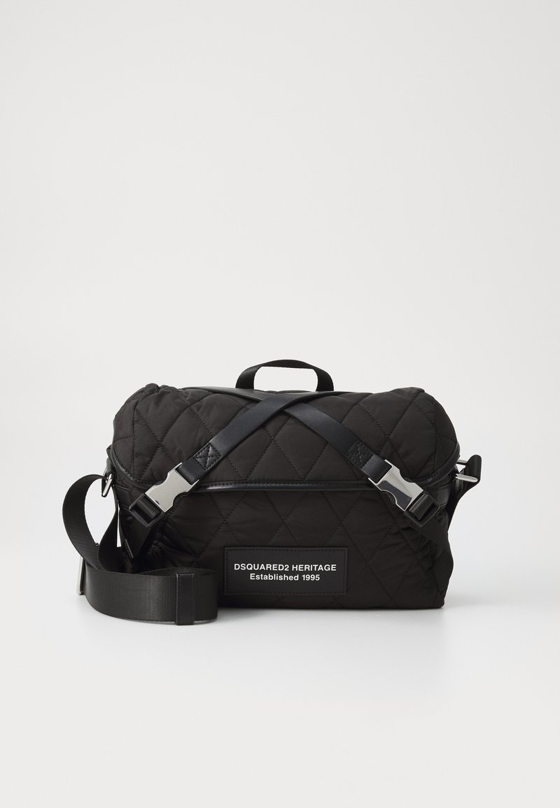 Black quilted shoulder bag with cross-body straps, featuring a rectangular shape and a branded patch. Smooth texture, silver hardware accents.