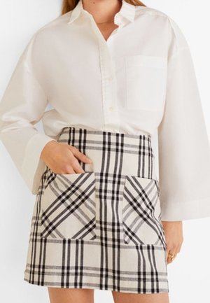 Camicia bianca a maniche lunghe con bottoni abbinata a una mini gonna scozzese con grandi tasche frontali in una combinazione di colori beige, nero e grigio.
