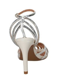 Sandalo con tacchi alti dalla base color crema, dettagli in strass argentati, con apertura sul retro e sottile cinturino alla caviglia. Design elegante e curvo.