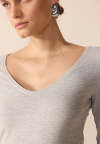 Top gris de manga larga con un diseño de cuello en V, hecho de una tela suave y texturizada, que presenta un sutil patrón jaspeado.