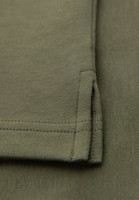 Olivgrön bomullstyg med en slät textur, med en prydligt sydd fåll och subtil söm som betonar den rena finishen och formen.