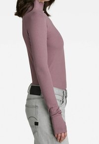 Ribbad, slim-fit långärmad topp i mauve med hög hals. Kombinerad med ljusgrå byxor med sidofickor och svarta detaljer vid midjan.