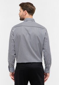 Camicia a righe con sottili righe verticali bianche e nere, maniche lunghe, polsini con bottoni e colletto tradizionale. Vista posteriore mostrata.