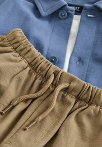 Camisa azul con botones, cuello y dos botones, combinada con pantalones caqui con cintura elástica y cordón trenzado.