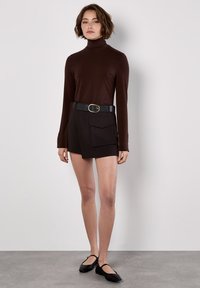 Brun åtsittande polotröja kombinerad med högmidjade svarta shorts som har en framficka och ett svart bälte med en rund metallspänne.