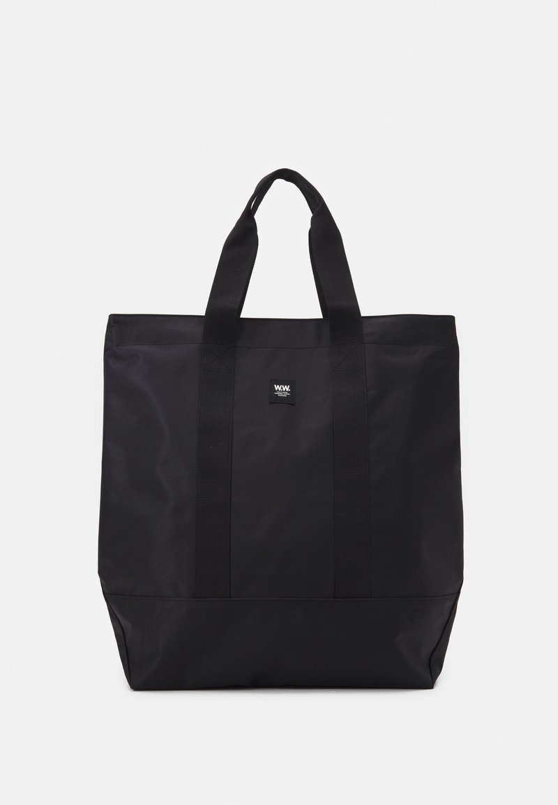Black tote bag made of durable fabric, featuring two fabric handles, a rectangular shape, and a small logo tag on the front.