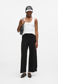 Fehér bordás ujjatlan felső, fekete, bő szabású nadrág, fekete-fehér sapka, kis fekete kézitáska, és fekete, pántos cipő. Egyszerű, minimál stílus.