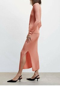 Ensemble deux pièces en tricot corail côtelé comprenant un haut à manches longues et une jupe avec une fente haute, associé à des escarpins noirs à bout pointu.