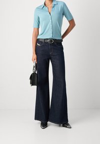 Camicia azzurro chiaro a maniche corte con bottoni, jeans a gamba larga blu scuro, cintura nera e borsa. Tessuto strutturato con scarpe nere lucide.