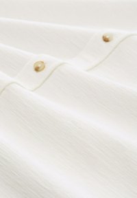 Witte shirt met een gestructureerd oppervlak, voorzien van twee goudkleurige knopen en een casual ontwerp. Lichtgewicht stof, subtiel lijnpatroon.