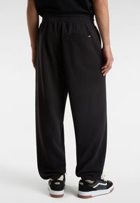 Černé tepláky s volným střihem, s elastickým pasem a zadní kapsou, v kombinaci s černobílými teniskami.