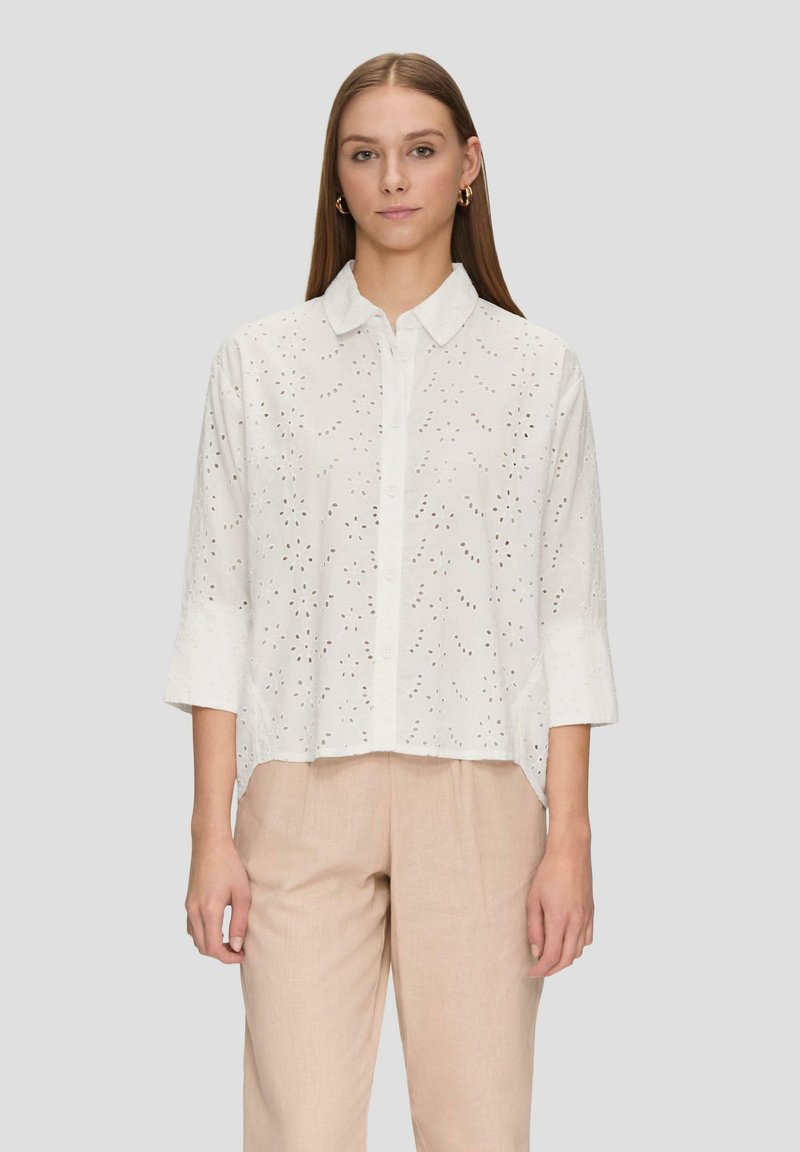 White button-up shirt with short sleeves, featuring eyelet embroidery, relaxed fit, and a collar. Pants are beige, made of a lightweight fabric.