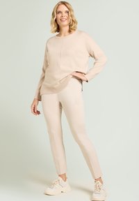 Suéter beige con cuello redondo y dobladillo acanalado combinado con pantalones de punto a juego. Se lleva con zapatillas de color claro. Diseño sencillo y depurado.