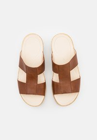 Brune lædersandal med brede krydsremme, teksturerede indersåler og en lysefarvet sål. Enkel, åben design for nem påføring.