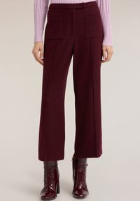 Bordowe spodnie o szerokich nogawkach wykonane z teksturowanej tkaniny, z dwoma przednimi kieszeniami. Noszone z jasnofioletowym prążkowanym topem i błyszczącymi botkami.