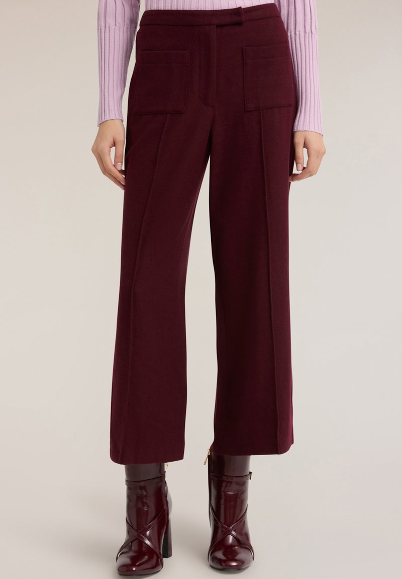 Bordowe spodnie o szerokich nogawkach wykonane z teksturowanej tkaniny, z dwoma przednimi kieszeniami. Noszone z jasnofioletowym prążkowanym topem i błyszczącymi botkami.