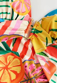 Farverigt stof med citrus- og blomstermønstre i levende pink, orange og gul, med samlet detaljer og guldhardware accenter.