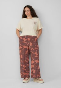 Crème oversized t-shirt met zonafbeelding; roestkleurige wijde broek met abstracte bruine patronen; tan platform sandalen.