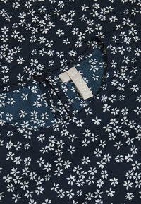 Námořnická blůza s květinovým vzorem a bílými malými květy. Má kulatý výstřih a zapínání na knoflíky s textilním štítkem s nápisem "PIECES."