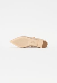 Chaussure nude à bout pointu avec une tige en suède lisse, un talon plat, une semelle intérieure texturée, et une sangle décorative ornée de petites perles.