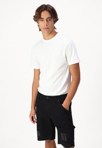 Camiseta blanca de manga corta combinada con pantalones cortos de denim negros con parches desgastados y bolsillos laterales. Diseño simple y limpio.