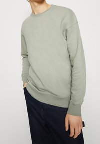 Grijs-groene oversized sweatshirt met een ronde hals, geribbelde manchetten en zoom, gecombineerd met donkere denim jeans. Gladde stoftextuur.