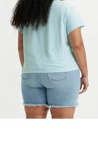 Svetle modré tričko s krátkým rukávem v kombinaci se světlými džínovými šortkami s třepenými okraji. Tričko má volný střih a šortky mají náprsní kapsy.